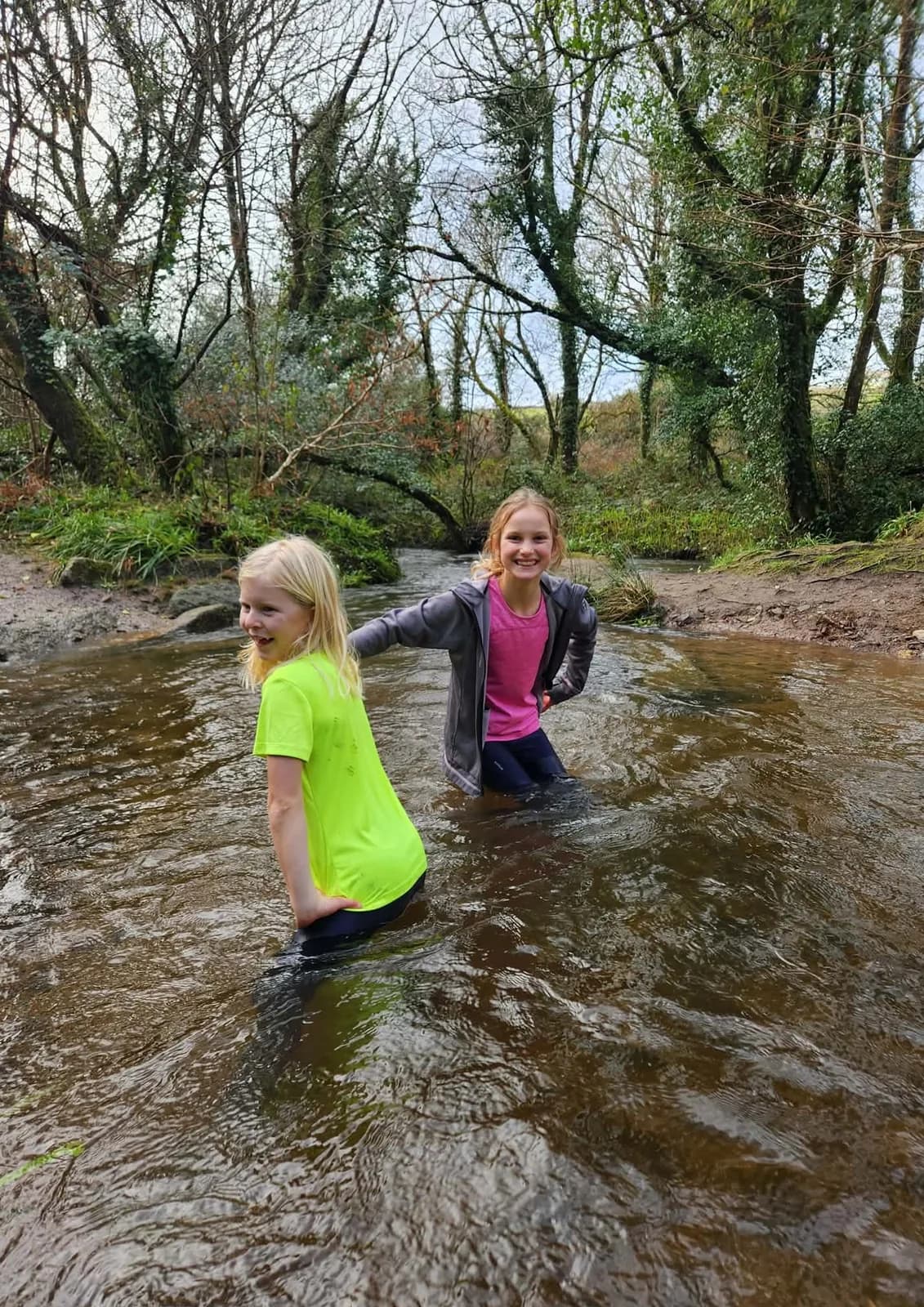 Two girls wading up a shallow river