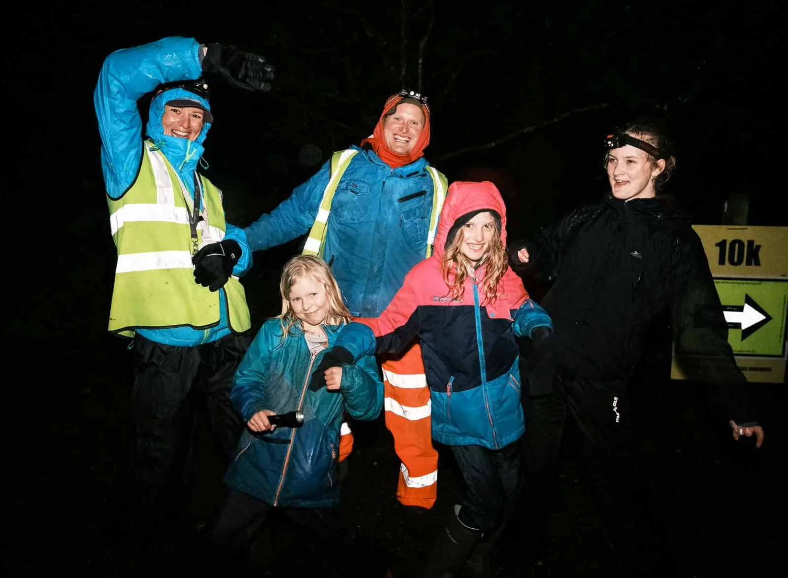 Families gathered at night around a lit 10k event sign