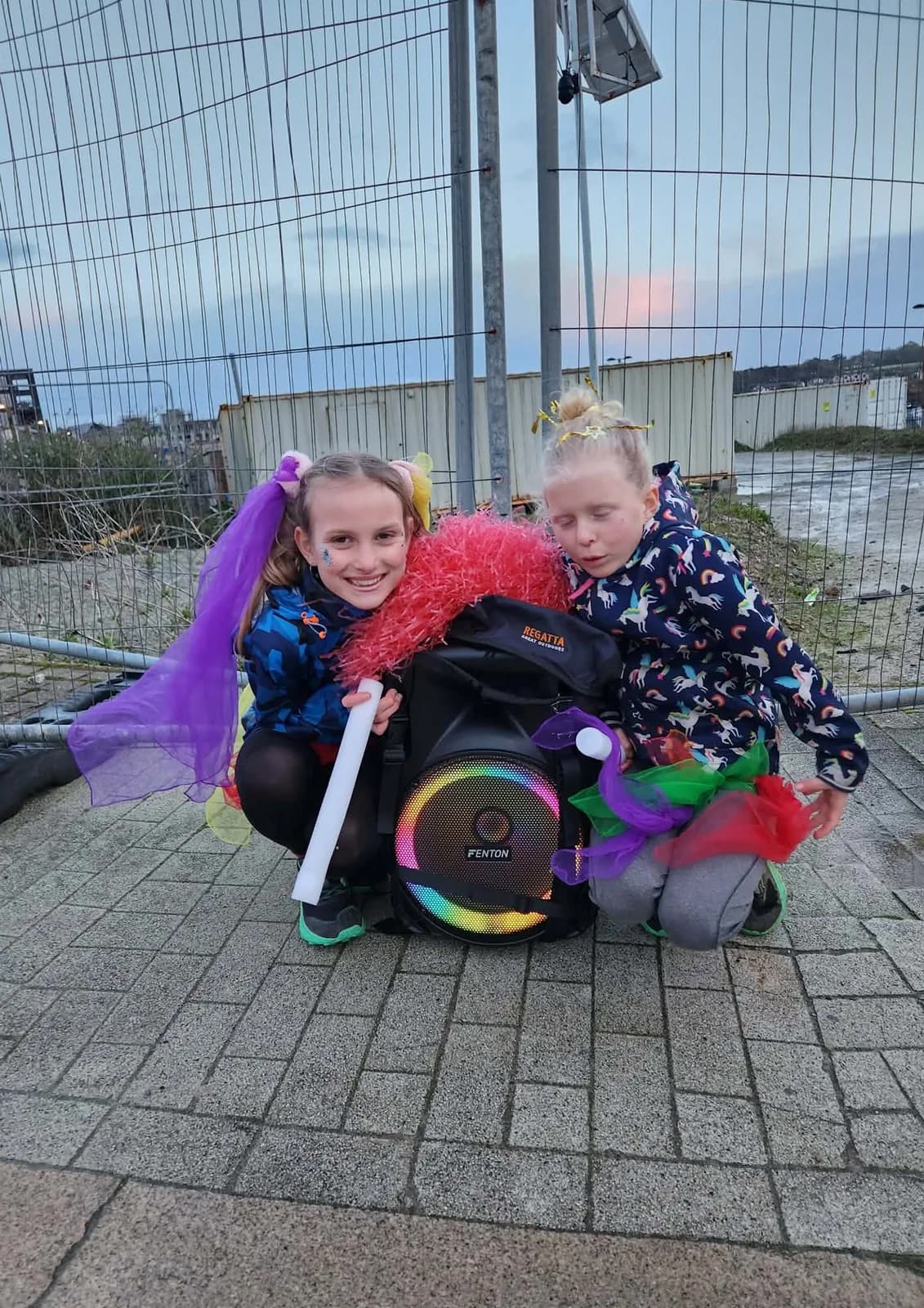 Two girls carrying a speaker box between them at dusk