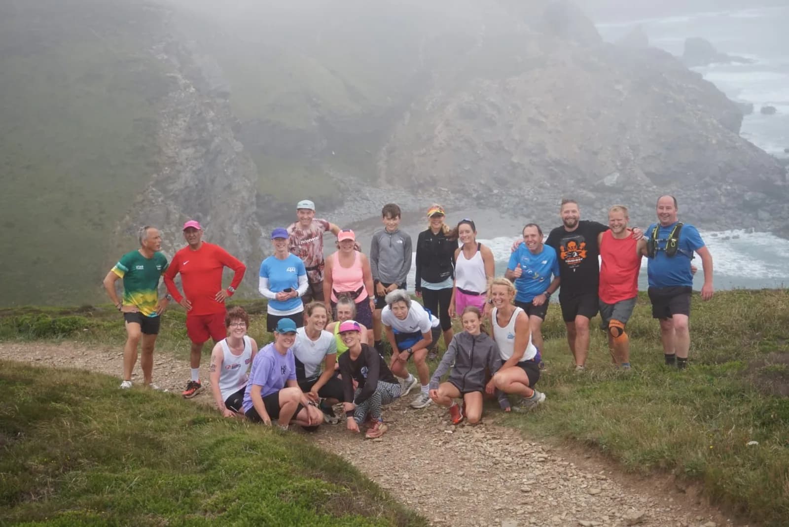 A group running the coast path above a misty cove