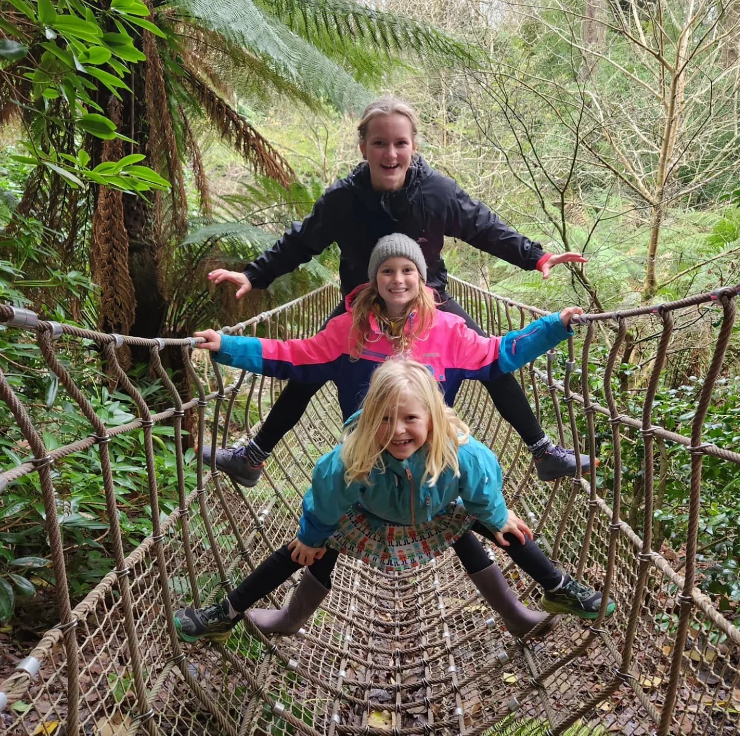 Two girls crossing a rope bridge in the trees, one steadying the other